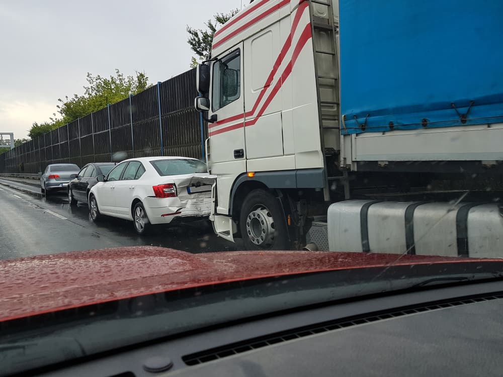 Highway car incident involving a passing car and a truck colliding with a passenger car in rainy conditions