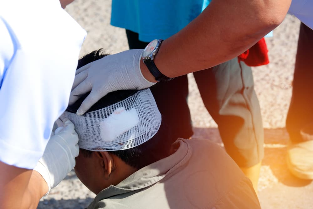 Man receiving first aid after a car accident, close-up of hands applying bandages to head injury.