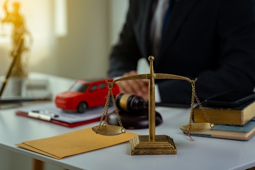 A close-up of a lawyer's desk with a scale of justice, a gavel, and a toy car. The scene symbolizes legal representation for car accident cases.