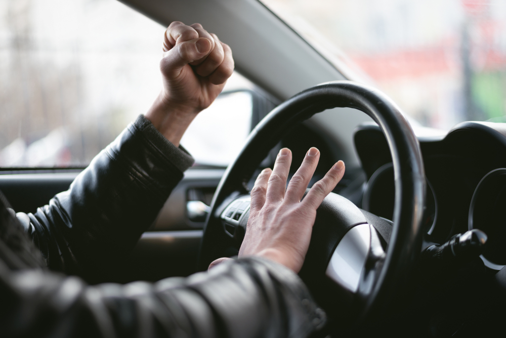 Angry driver is honking and is yelling by sitting of a steering wheel. Road aggression concept.