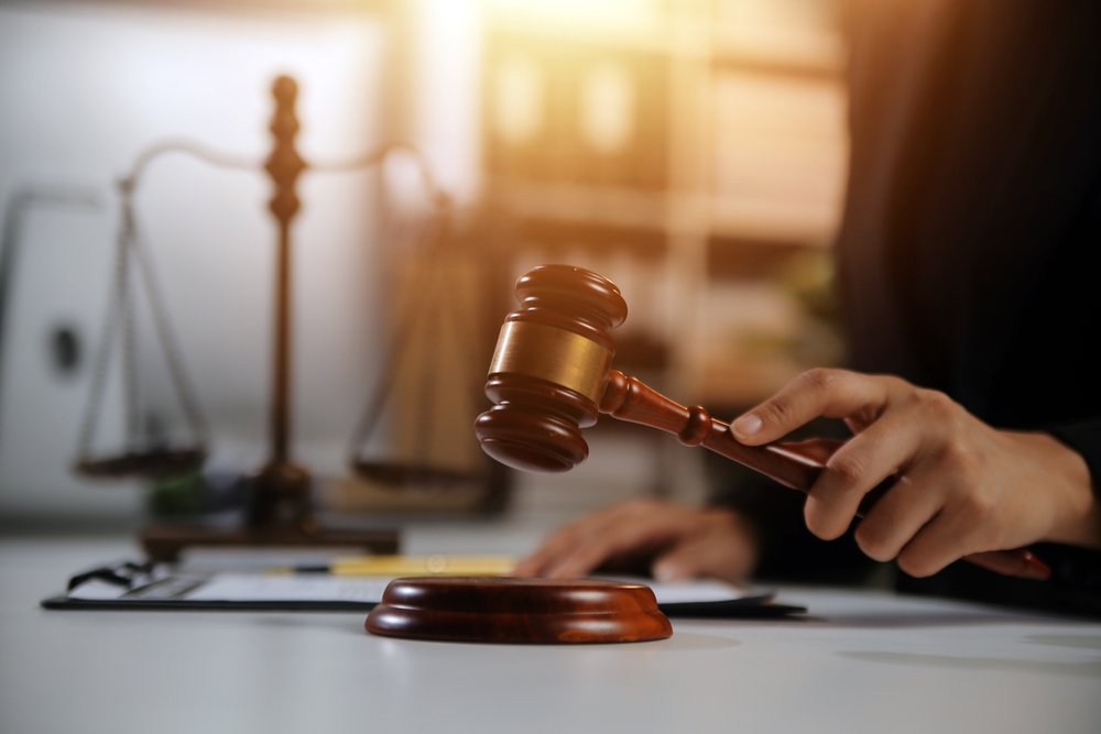 A lawyer or legal professional holding a wooden gavel above a desk, with legal scales and documents in the background.